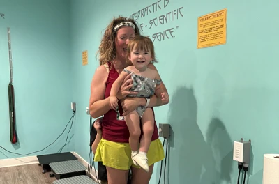 An adult holding a baby inside a clinic room, with light blue walls and instructional signs on the wall.